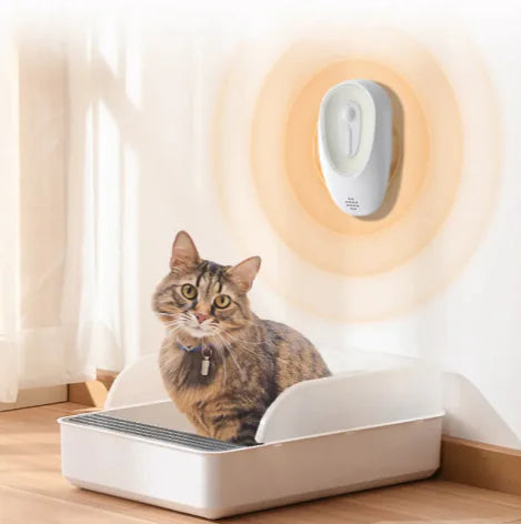 Cat using litter box with odor eliminator device on wall, maintaining a fresh environment. Focus keyword: litter box odor eliminator.