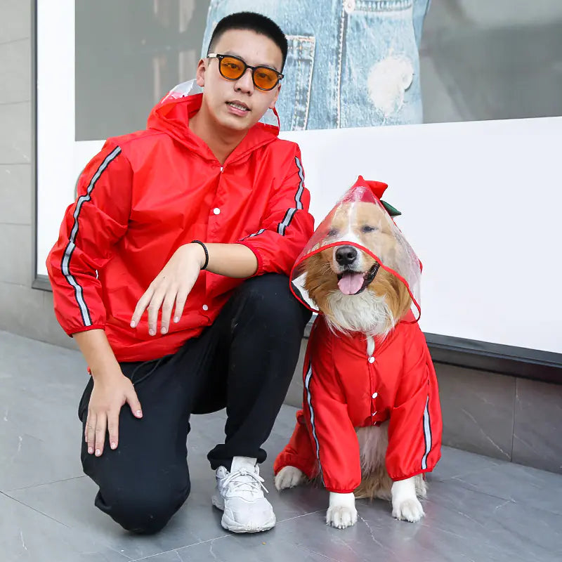 Pet and owner wearing matching red all-weather pet raincoat for outdoor protection.
